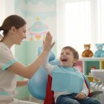 Dottoressa dentista che batta il cinque con il suo piccolo paziente sorridente